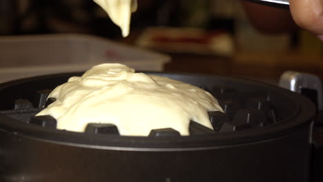 spreading waffle batter on a waffle iron for a homemade breakfast - isolated close up