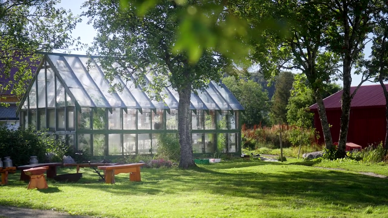 Ein Glashaus-Veranstaltungsort steht in einem sonnigen Garten auf Kvitnes Gaard, Norwegen.