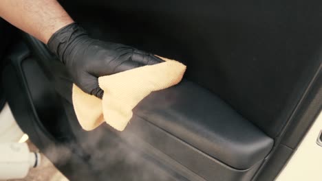 male wearing black gloves cleaning a car door interior with steam