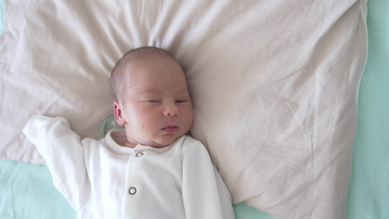 Cute baby is slowly falling asleep. He blinks his eyes and smiles a little. Sleepy sweet child look from above.