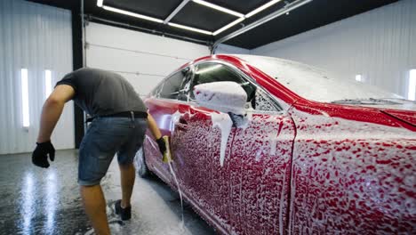 man worker washing red car on a car wash with yellow washcloth.