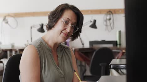 portrait of happy caucasian female worker with glasses writing in jewellery studio in slow motion