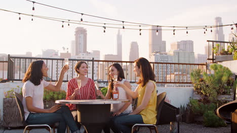 Amigas-Haciendo-Un-Brindis-Para-Celebrar-En-La-Terraza-De-La-Azotea-Con-El-Horizonte-De-La-Ciudad-En-Segundo-Plano.