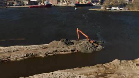 panning drone shot of excavator digging through ground surrounded by water