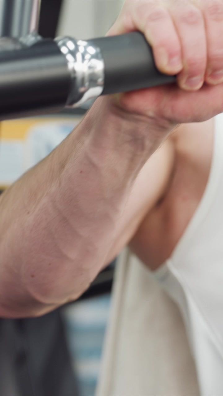 İç mekan fitness seansı sırasında siyah dolgulu halter veya makine parçasını sıkıca kavrayan erkek elinin yakın çekimi. Odak, yumuşak aydınlatma ile kavrama detayı ve dokusu üzerinde sabit kalıyor.