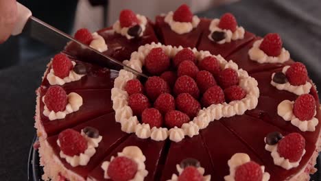 a young girl slowly cuts the cake decorated with raspberries