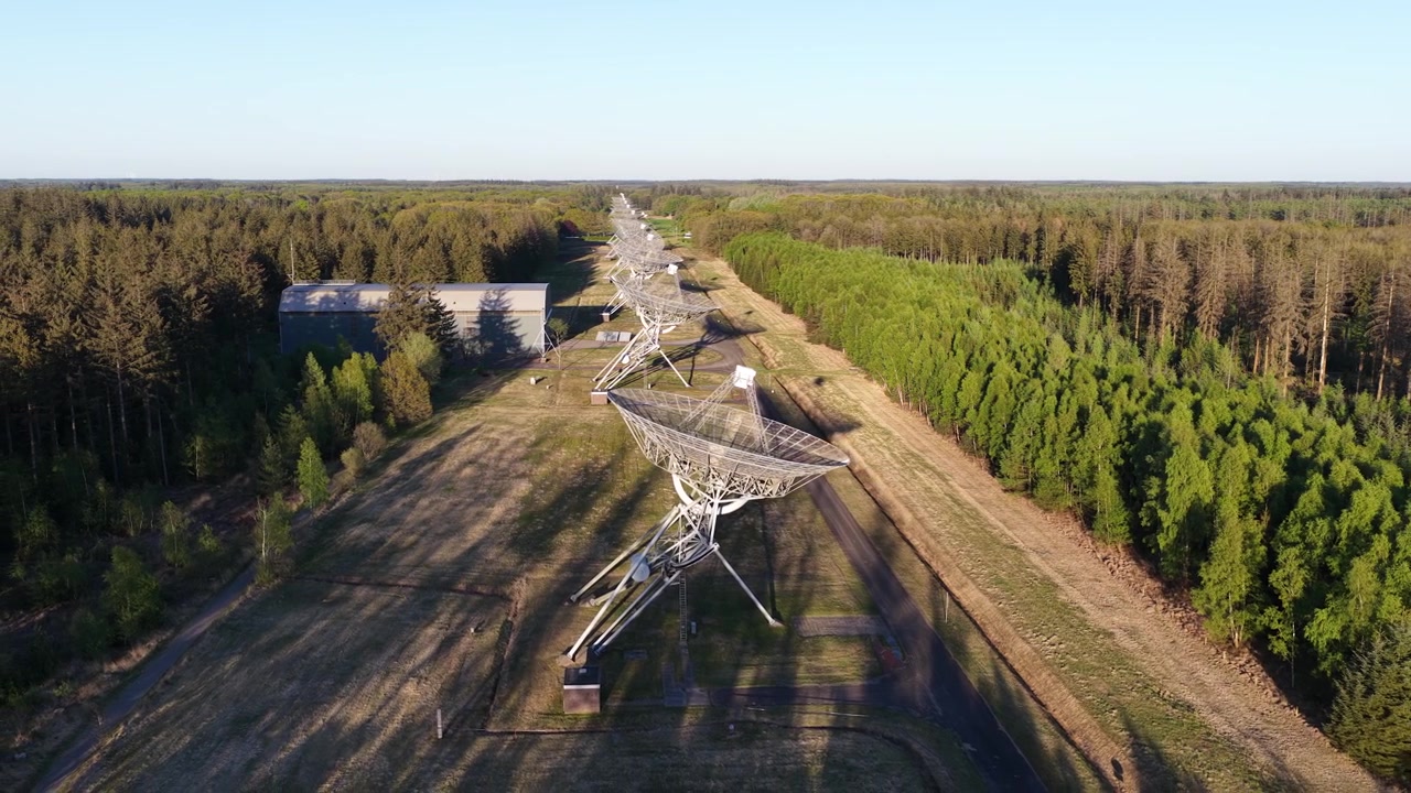 Вид с воздуха на радиотелескоп Westerbork Synthesis Radio Telescope в лесной прогалине в Нидерландах на закате, спутниковые антенны отбрасывают длинные тени на ландшафт