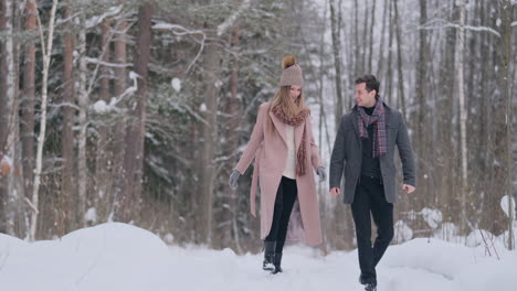 Young-married-couple-in-love-walking-in-the-winter-forest.-A-man-and-a-woman-look-at-each-other-laughing-and-smiling-in-slow-motion.-Valentine's-Day-love-story.