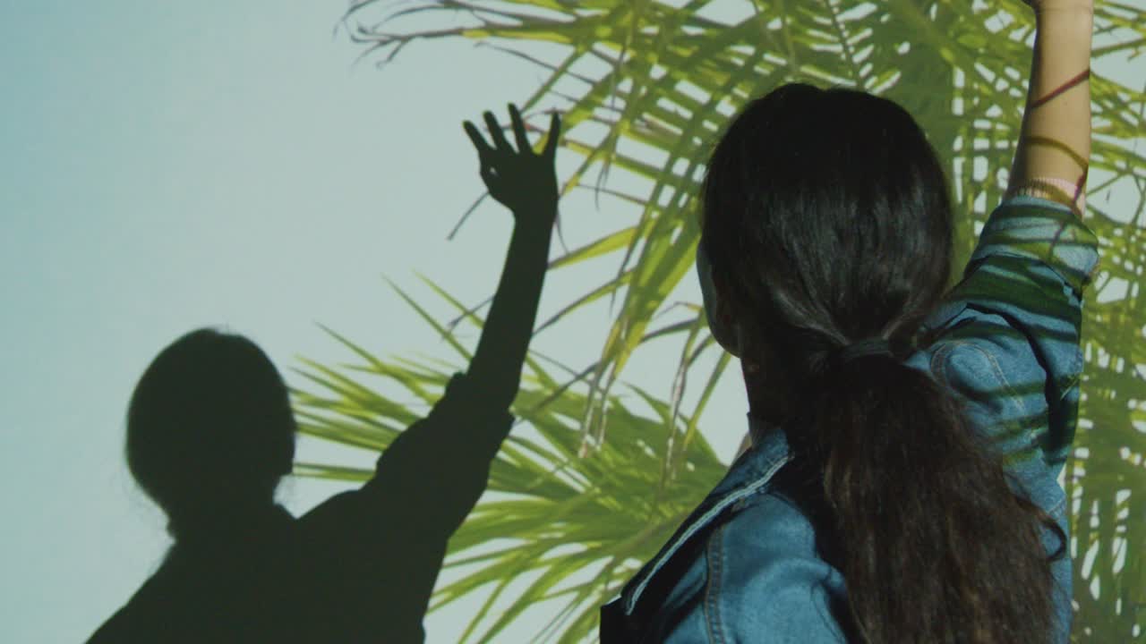 몰입 예술 전시회를 방문하는 여성은 그녀의 몸에 투사되는 종려나무 잎의 이미지와 상호 작용합니다.