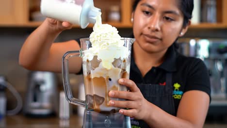 a skillful barista creates a frosty beverage by layering cream, coffee, and ice in a blender, showcasing the art of beverage preparation with precision and care