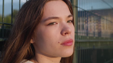 young lady leans on stadium fence at sunset. woman athlete relaxes after workout thinking about loneliness. sunny evening for solitude with thoughts