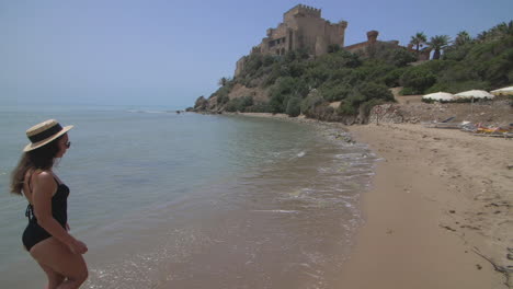 woman in a black swimsuit on a beach with a castle in the background