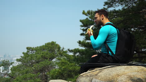 man hiker eating banana sitting on mountain peak - slow motion side view