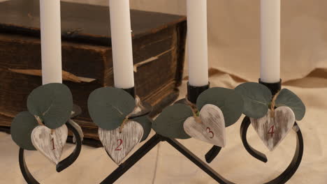 Slow-tilt-up-of-four-numbered-lit-candles-by-old-heavy-book,-close-up