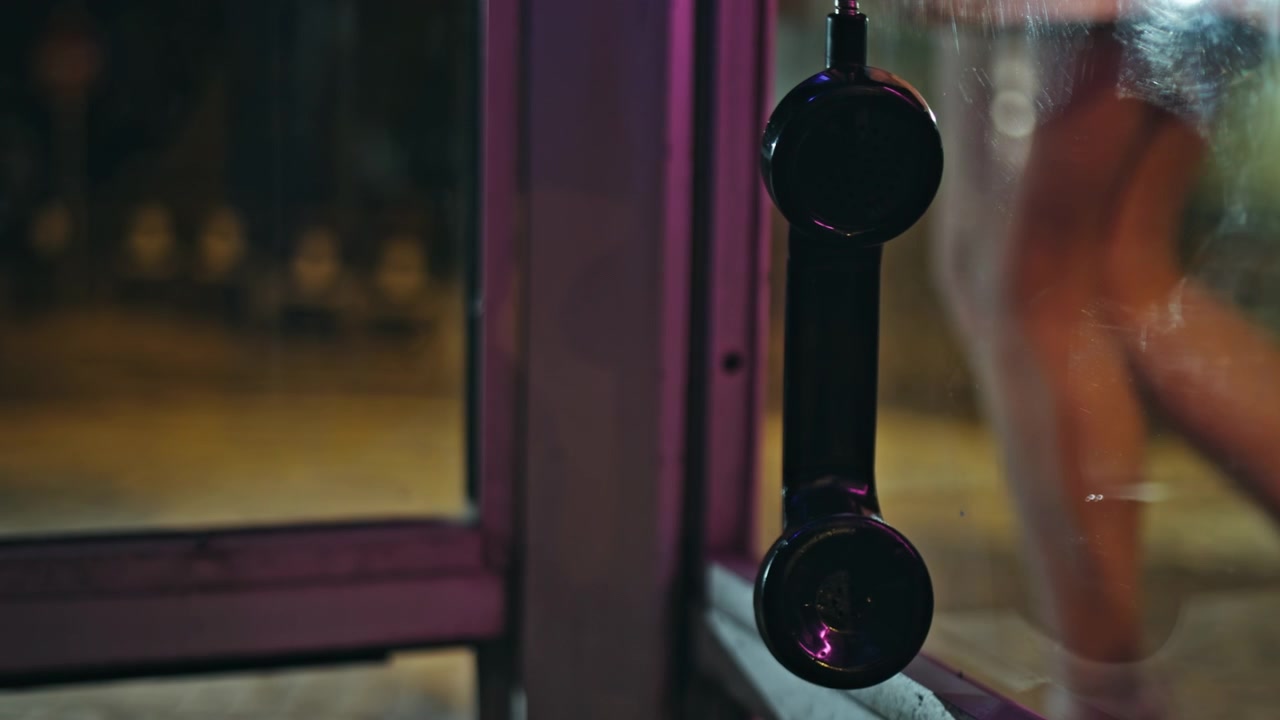 Closeup receiver hanging payphone night. Neon street telephone, woman walking.