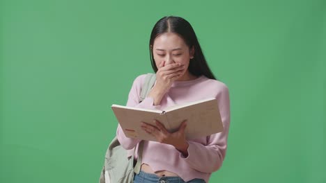 아시아 여학생이 책을 읽고 녹색 스크린 스튜디오에서 걱거리고 있습니다.