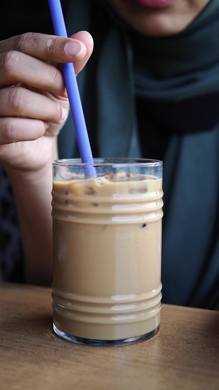 Donna che beve caffè freddo con una cannuccia in un bar