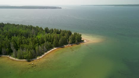 aerial descent to island tip with forested area and beach, lake huron, michigan