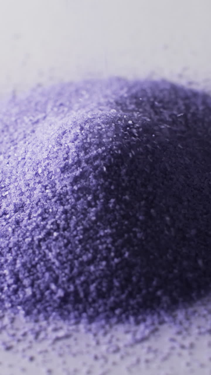 Vertical video of close up of heap of purple sand grains and copy space on white background
