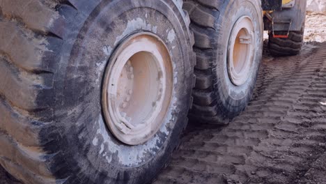 close-up of large, muddy wheels on an industrial vehicle against a rugged terrain