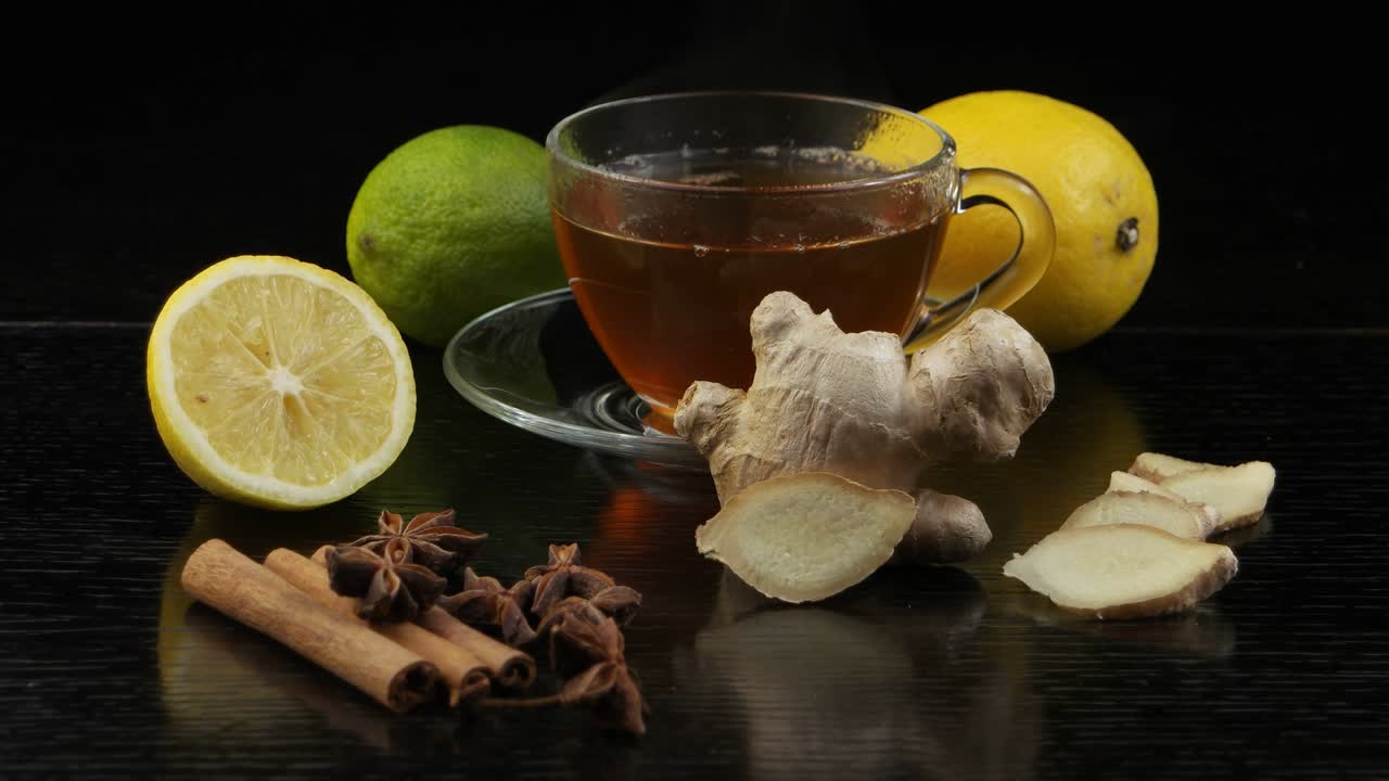 el vapor se eleva por encima de una taza de té caliente. limón, lima y especias para el té en una mesa de madera negra