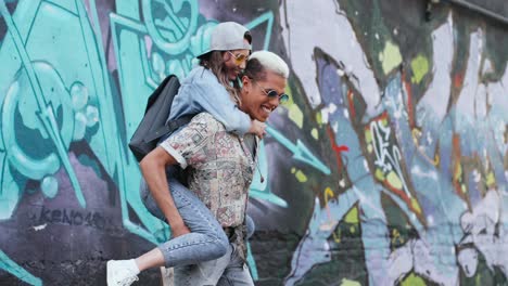 un joven que le da a su novia un piggyback cerca de una pared de graffity en la calle