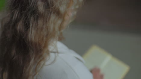 close up rear view of woman seated outdoors at night opening to new page of book in her hand as her curly hair sways gently in wind, slightly blurred for soft and tranquil visual atmosphere