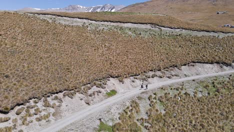 tres personas caminando por un sinuoso camino de tierra al lado de una montaña seca bajo el sol
