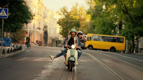 Happy-couple-guy-with-long-curly-hair-in-a-plaid-shirt-and-denim-jacket-rides-with-his-happy-brunette-girlfriend-in-a-plaid-shirt-on-a-moped,-the-girl-puts-her-arms-and-legs-forward-having-fun-and-rejoicing-while-riding-along-a-wide-street-with-her-boyfriend-in-the-summer-city