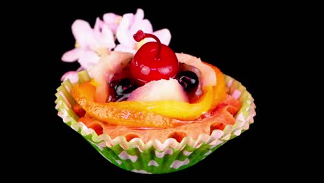 cream cupcake with cherry, berry, fruits and apple flowers on black background rotate slowly.