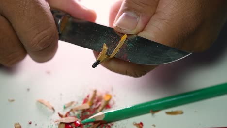 footage of hands slowly sharpening a pencil and some coloured pencils with a sharp knife