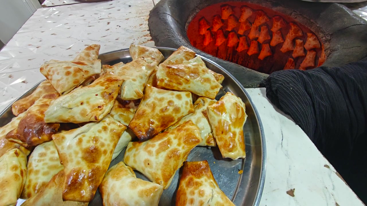 Fornaio che rimuove samsa appena sfornati da un tradizionale forno tandoor