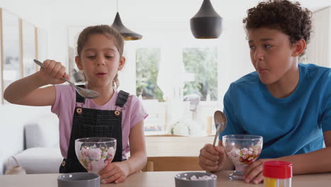 children in kitchen at home eating ice cream and pulling faces at each other