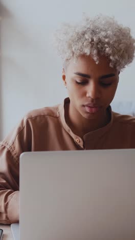 young overjoyed african american woman looks at laptop sits at table in office