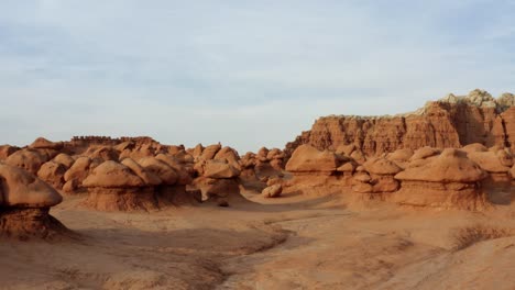 Gorgeous-stunning-aerial-drone-dolly-out-shot-of-the-beautiful-Goblin-Valley-Utah-State-Park-mushroom-rock-formations-with-red-and-white-Butte's-in-the-background-on-a-warm-sunny-summer-day