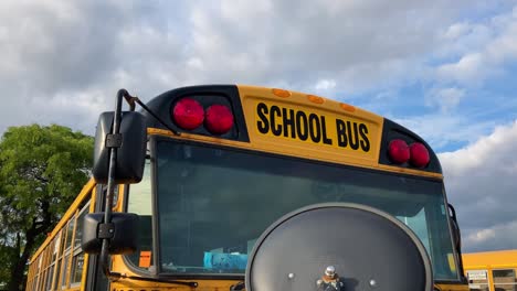 school bus close up circle left showing red lights and mirrors while parked