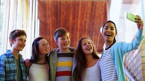 smiling schoolkids taking selfie with mobile phone in corridor