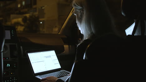 vista trasera de una mujer de negocios que usa una laptop en un auto por la noche