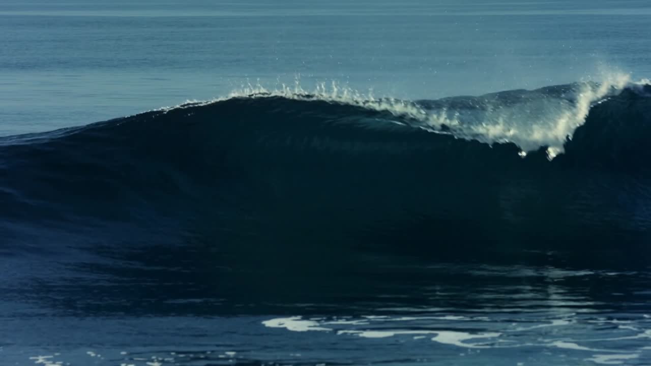 Rolling ocean swell approaching shore, steepening crest, curling lip, sending foam and spray