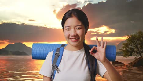 un close-up de una excursionista asiática con una mochila de montañismo sonriendo y mostrando un gesto de acuerdo a la cámara en un lago