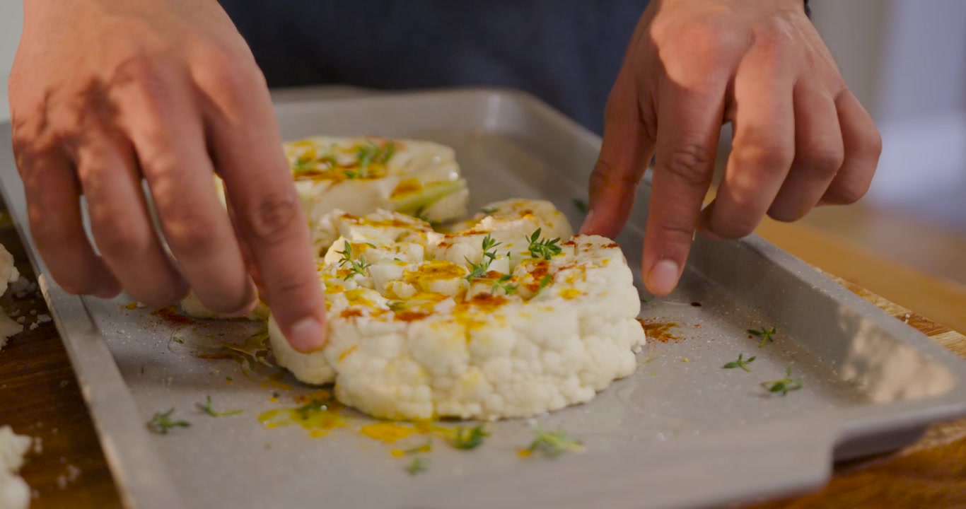 Donna afroamericana che, dopo un filo d'olio, sistema i pezzi di cavolfiore su una teglia in cucina per arrostirli.