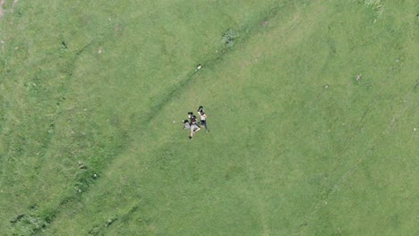 vista aérea de una pareja joven tumbada en un césped y relajándose después de una caminata agotadora a la iglesia de la trinidad de gergeti, georgia