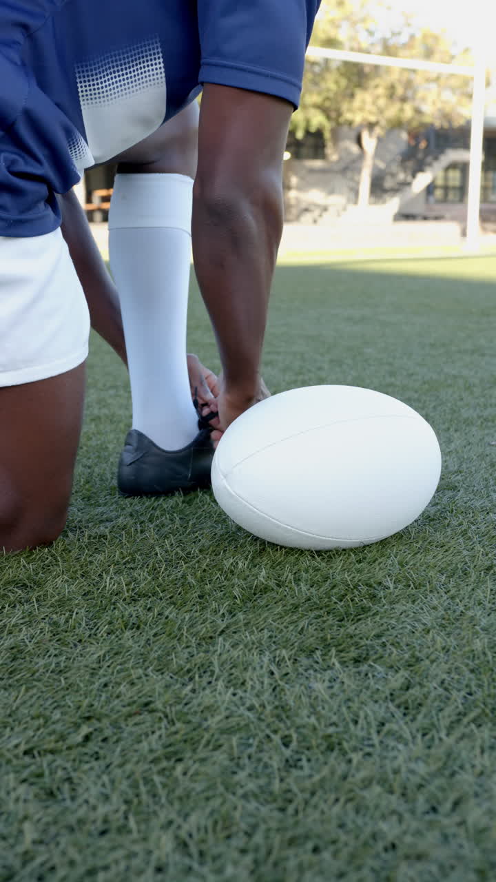 Vertical video: Athlete tying shoelaces on field, preparing for rugby practice outdoors