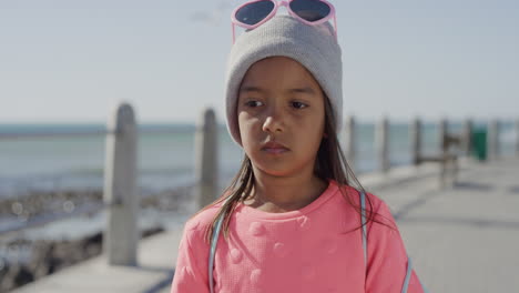 portrait sad little mixed race girl looking unhappy kid wearing pink on sunny seaside beach slow motion