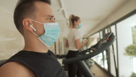 joven atleta masculino y femenino con mascarilla usando máquinas de ejercicio en el gimnasio