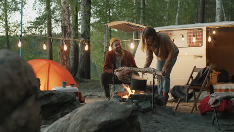 couple cooking food over campfire in evening