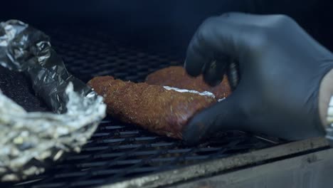 a chef places meat onto a bbq smoker grill and closes the lid