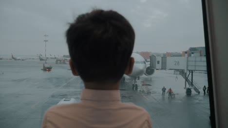 boy looking at plane in the window when waiting for his flight