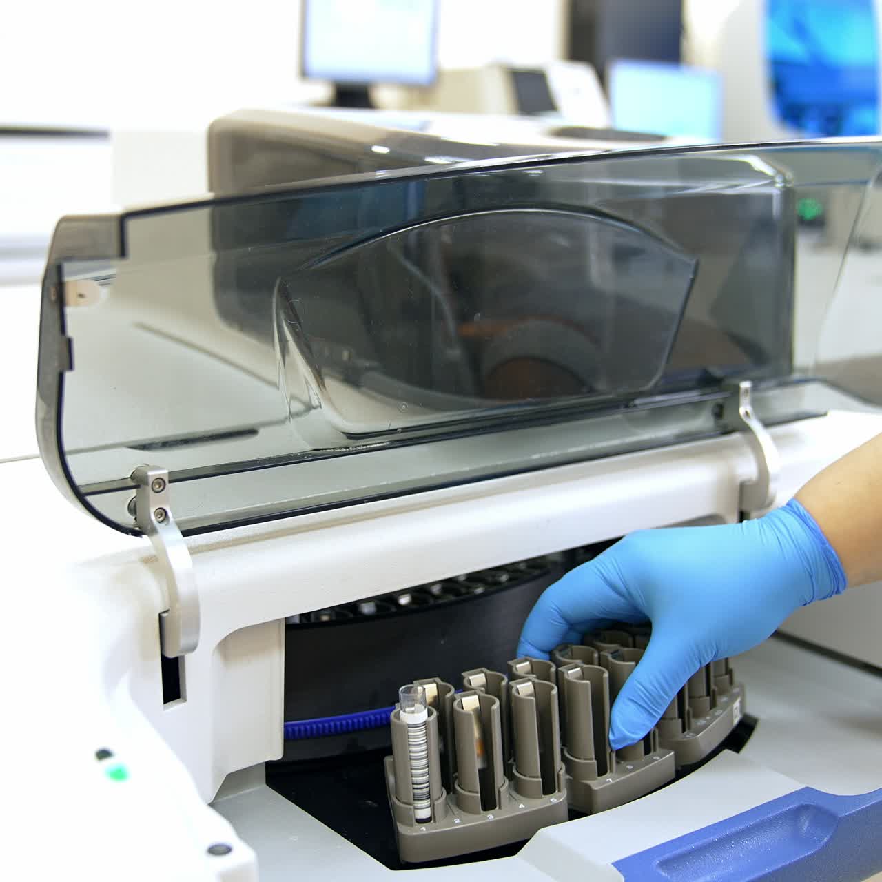 Medical laboratory assistant places a stand with a test tube into the machine. Female hand in gloves closes the lid in equipment to start the testing procedure