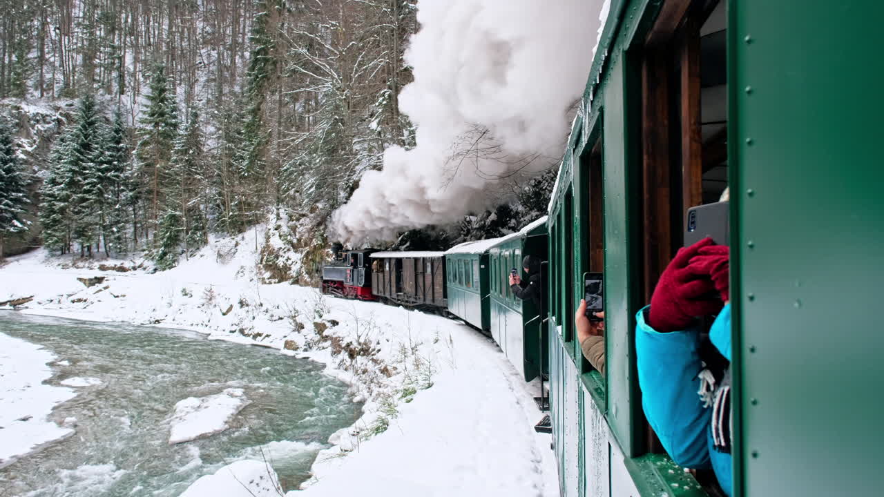 Näkymä liikkuvasta Mocănița-höyryjunasta sen sisältä, paljas metsä talvella, lunta, matkustajien kuvausta, Romania